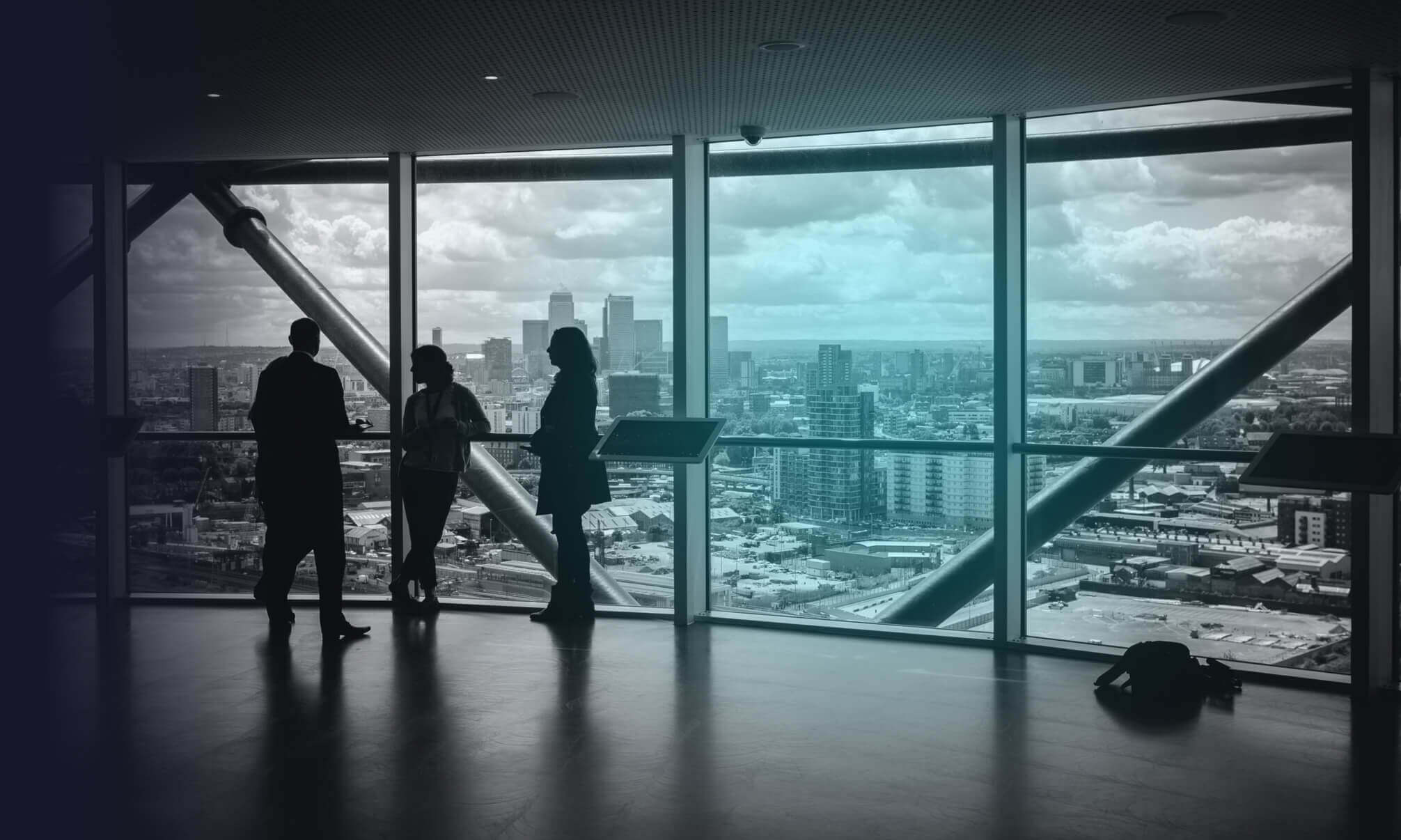 Four people are talking in a large building next to a glass wall with a view of a metropolitan city.