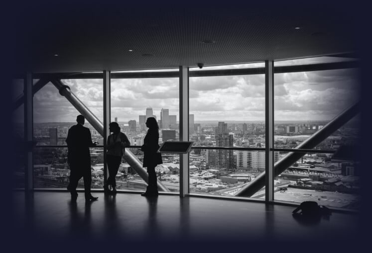 Four people are talking in a large building next to a glass wall with a view of a metropolitan city.